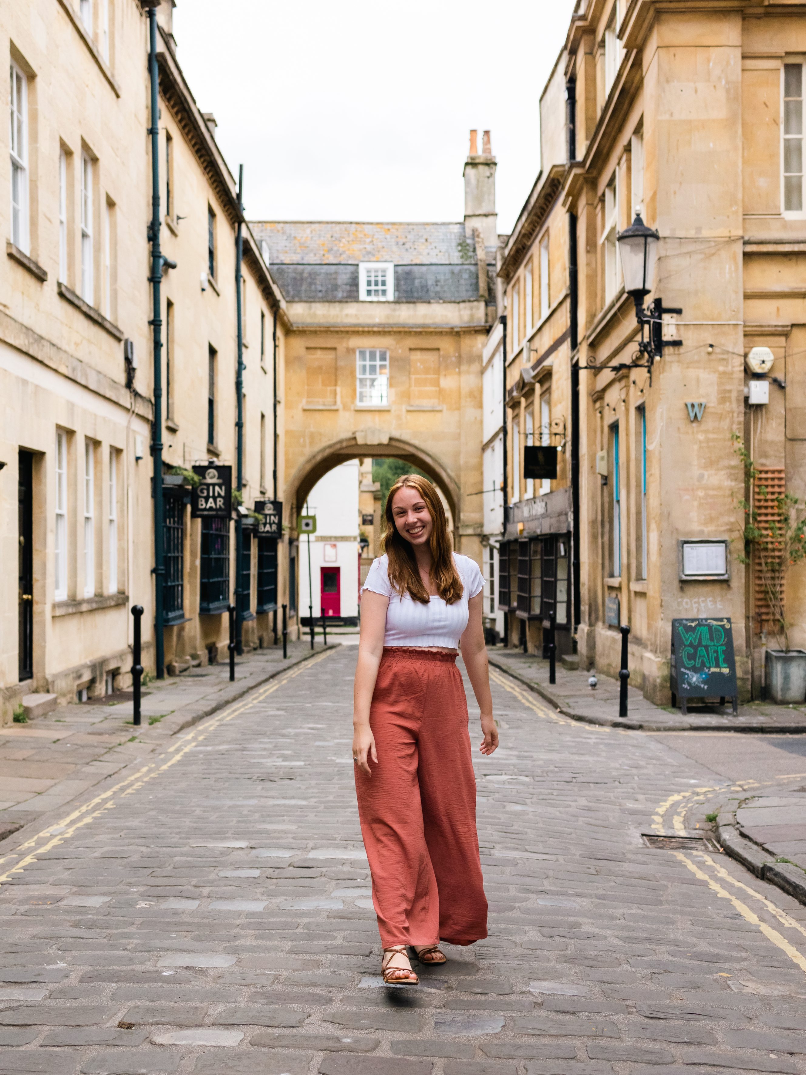 A girl walks down a stone street lined with tan buildings in Bath, England.