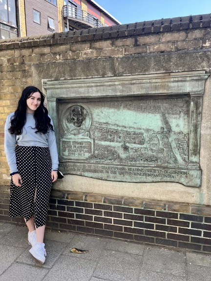A girl stands in front of a sign that commemorates the site of the original Globe Theatre in London, England.