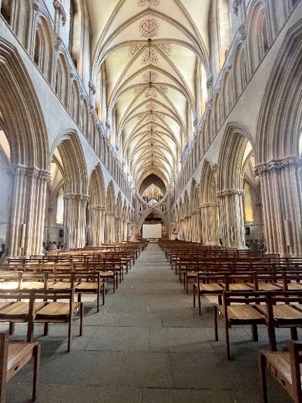 The inside of the Wells Cathedral shows high arches of white marble and rows of chairs.