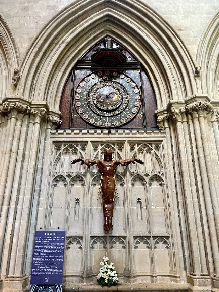 A large, ancient clock and a statue of Jesus Christ hang on the wall of the inside of the Wells Cathedral.