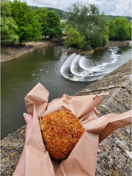 Scotch Egg held up in front of Pulteney Weir in Bath, England