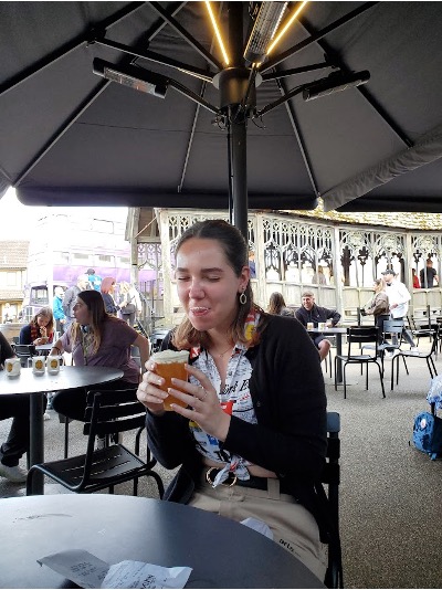 A girl sits at a table under an umbrella drinking butter beer